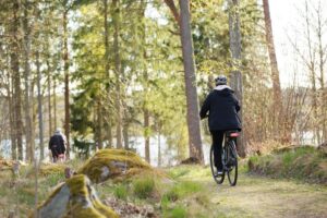 Kuvassa kaksi ihmistä pyöräilee metsäpolulla.