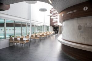 Kuvassa liikunta- ja uimahallin lipunmyyntitiski sekä aula, jossa pöytiä ja tuoleja.
